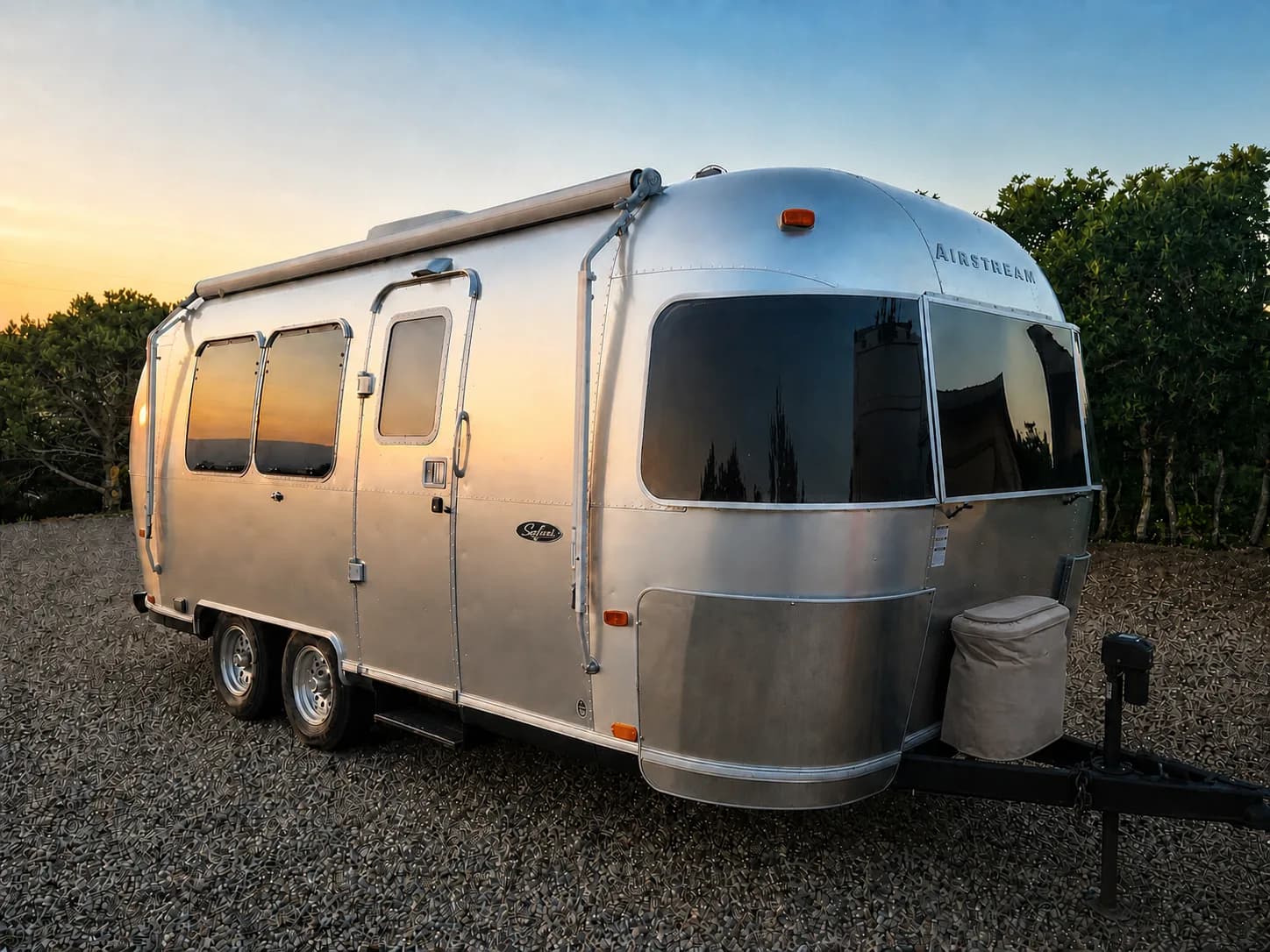Front three-quarter view of a silver Airstream Safari with its entry side, windows, and wheels visible